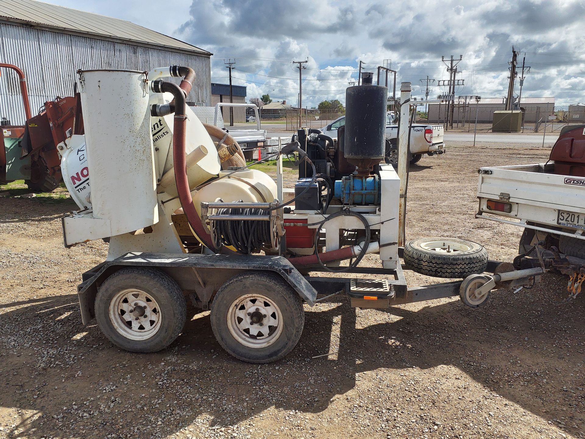 White and black road sealer machine on a trailer outdoors, with a tan silo.