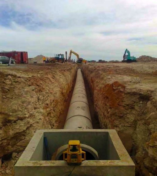 Concrete pipe laid in a construction trench with heavy machinery in the background.