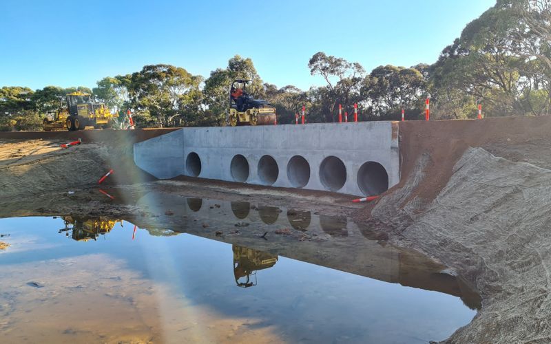 Concrete culvert with six openings over water, orange safety cones visible, sunny day.