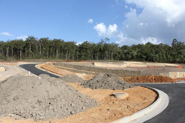 Construction site with graded earth, asphalt roads, and a treeline in the background.