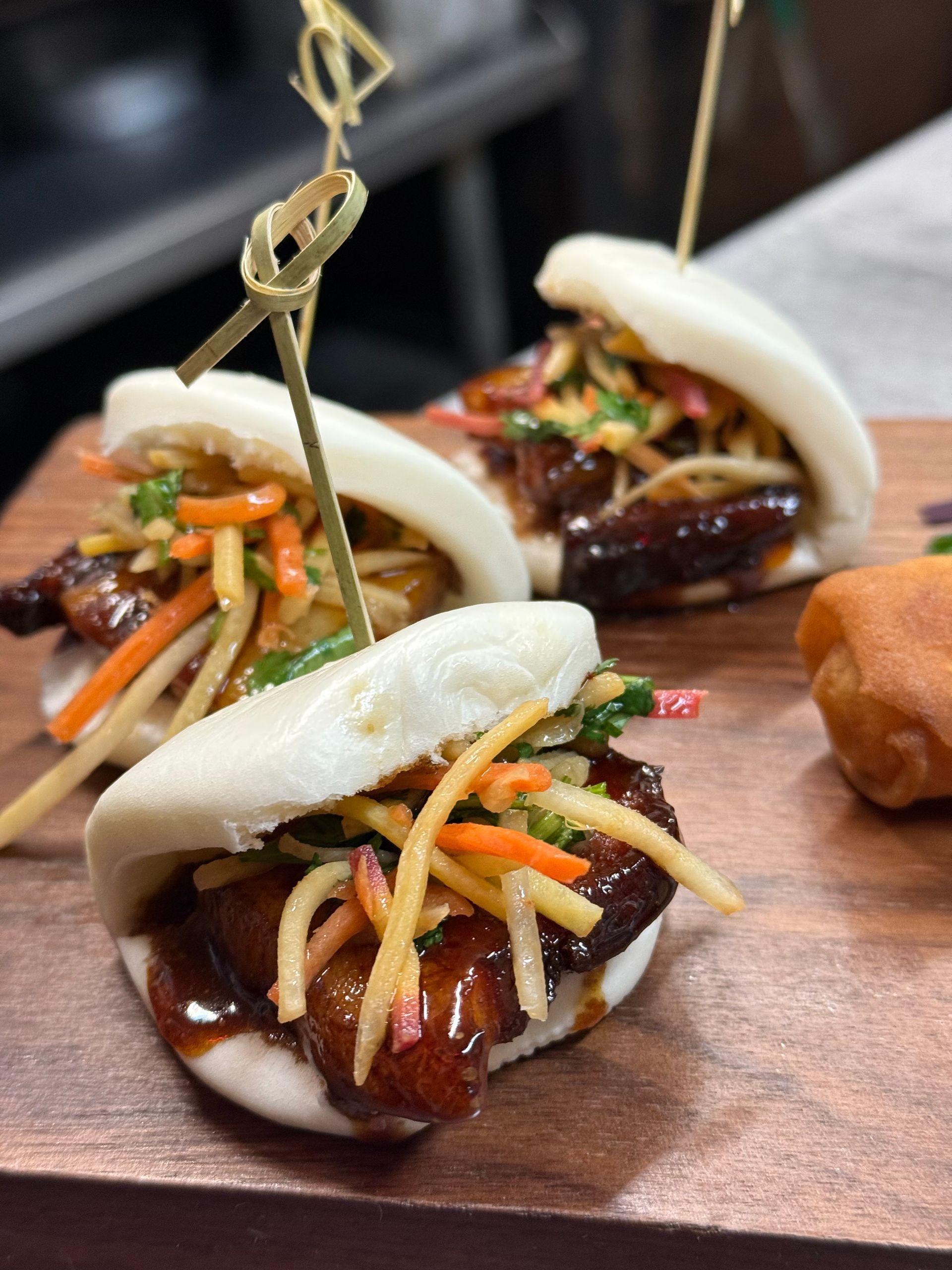 Three bao buns with meat and vegetables on a wooden cutting board
