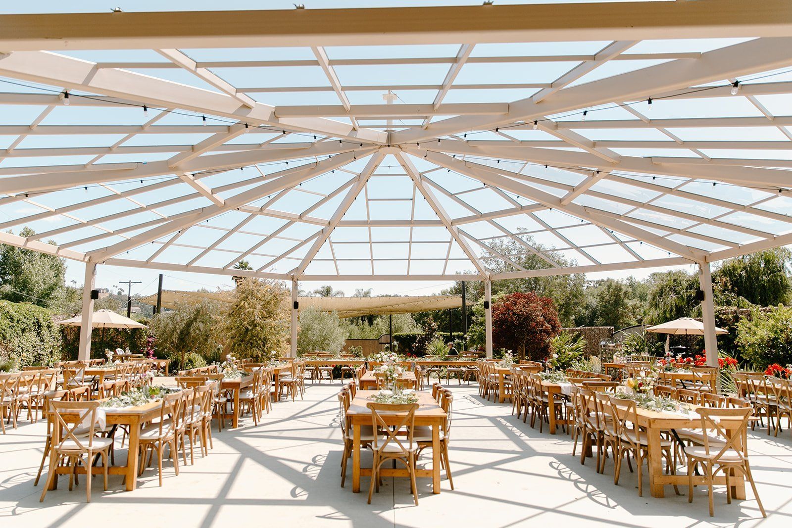 A large outdoor dining area with tables and chairs under a clear roof.