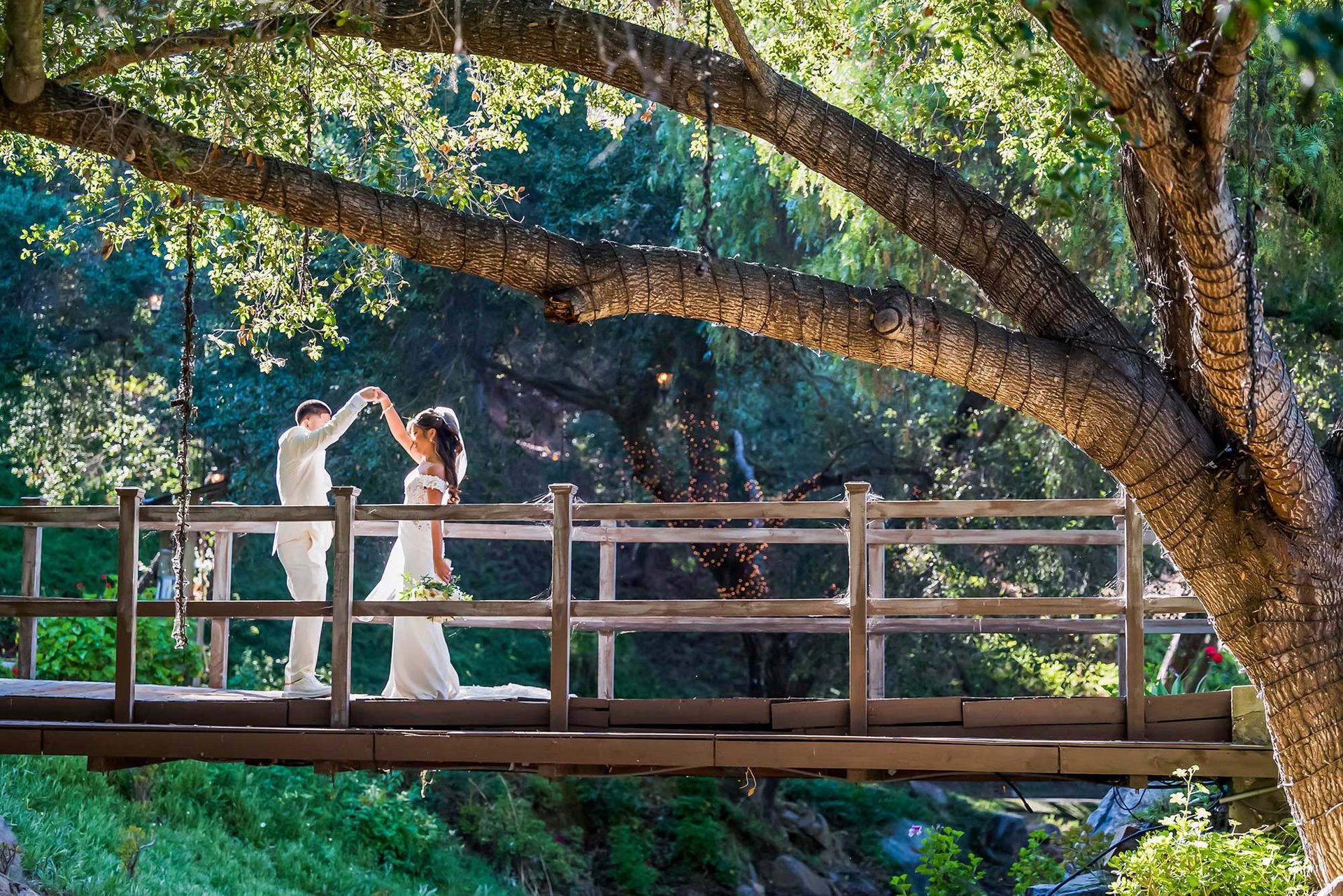 A bride and groom are dancing on a wooden bridge.
