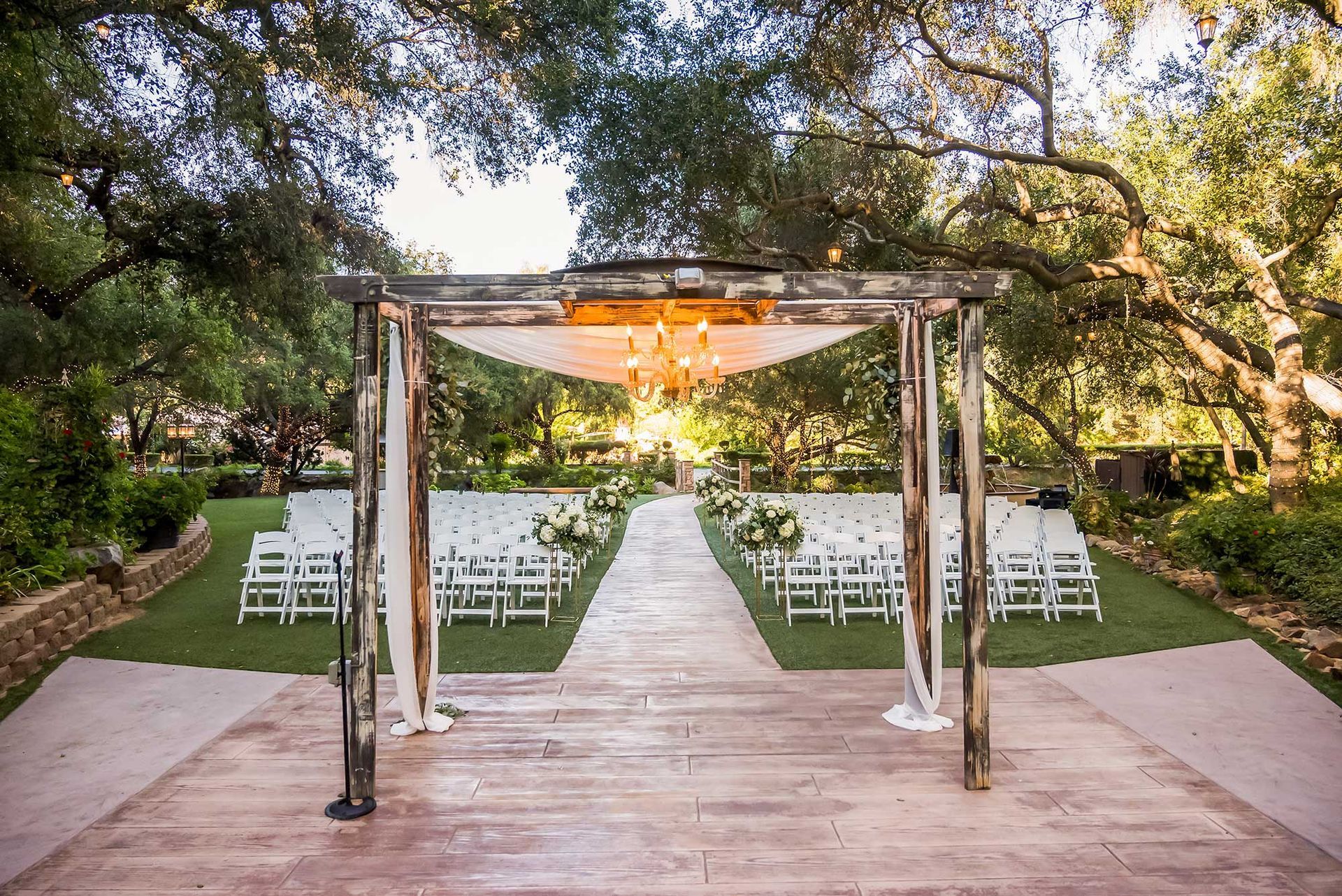 A wooden walkway leading to a wedding ceremony with white chairs under a canopy.