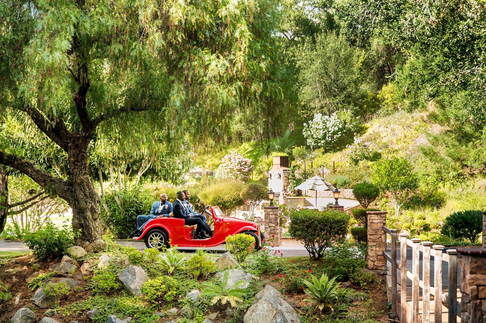 A group of people are riding in a red car through a park.