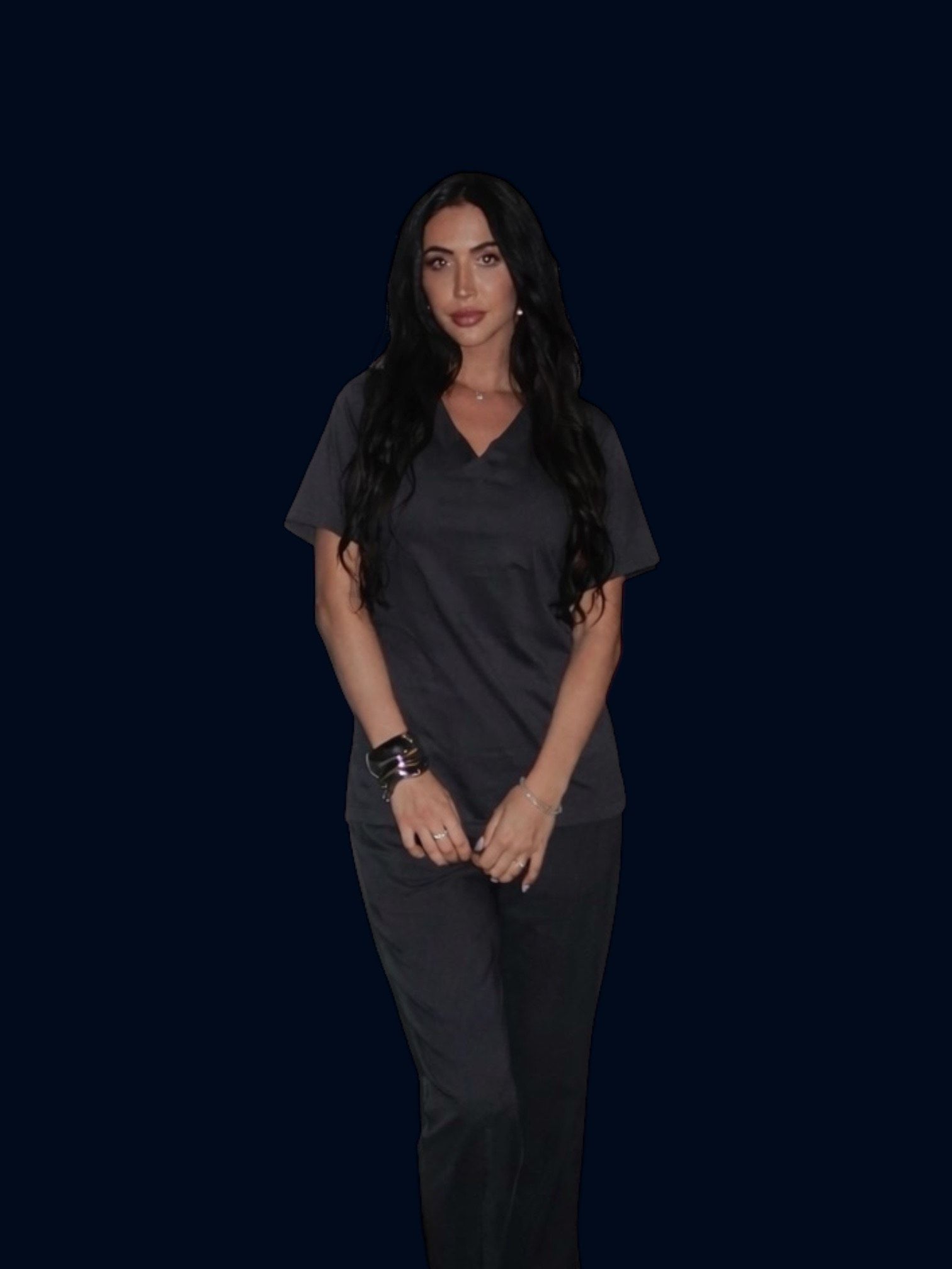 Woman in gray scrubs stands, hands clasped, dark hair, blue background.