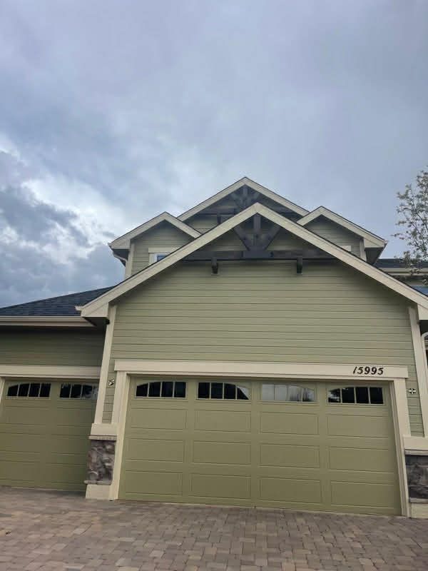 A two-story house with green horizontal siding, a light-colored trim, and a multi-car garage under a cloudy sky.