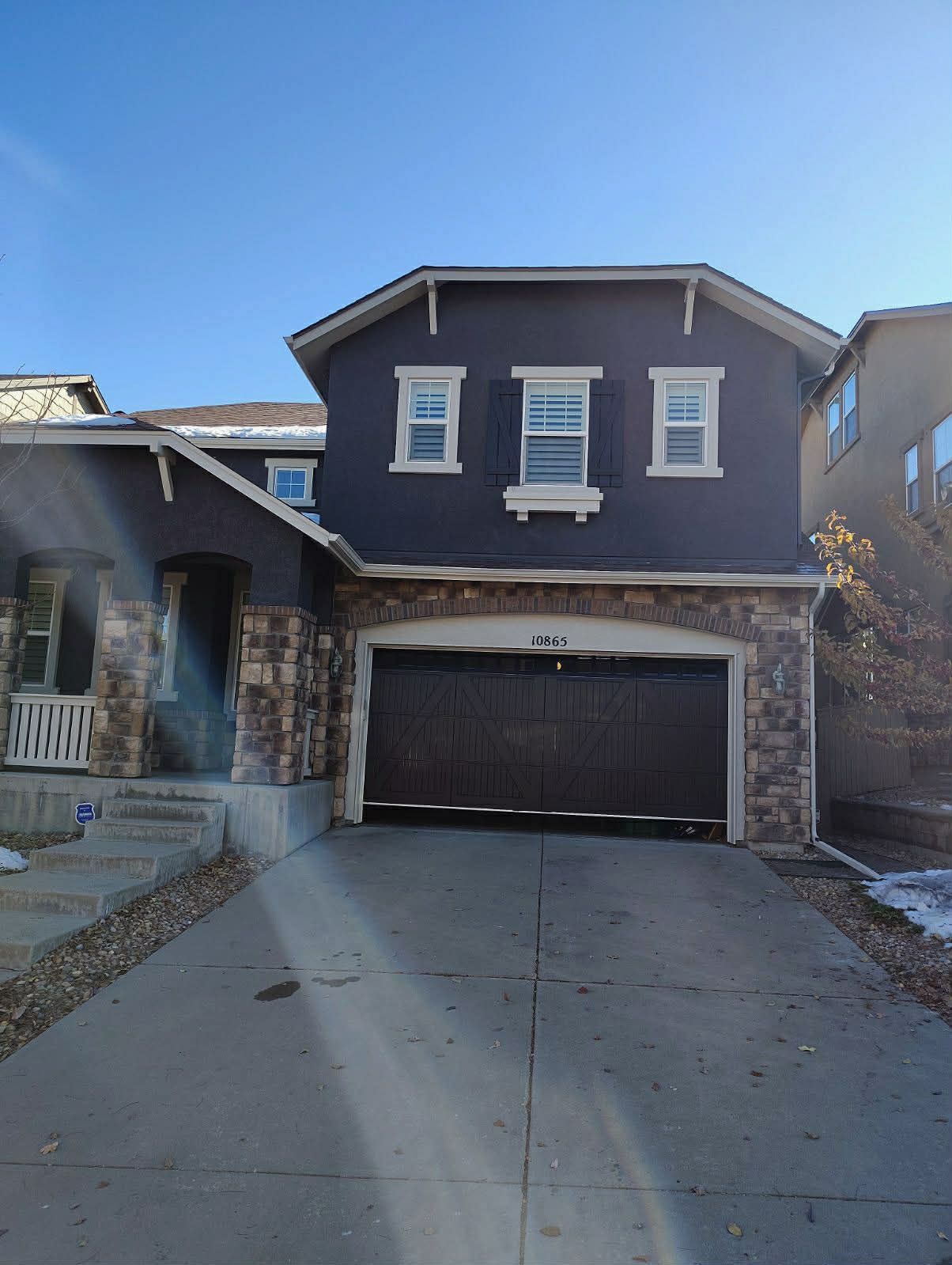 Two-story residential home with a dark gray exterior, stone facade, and a two-car garage on a paved driveway.