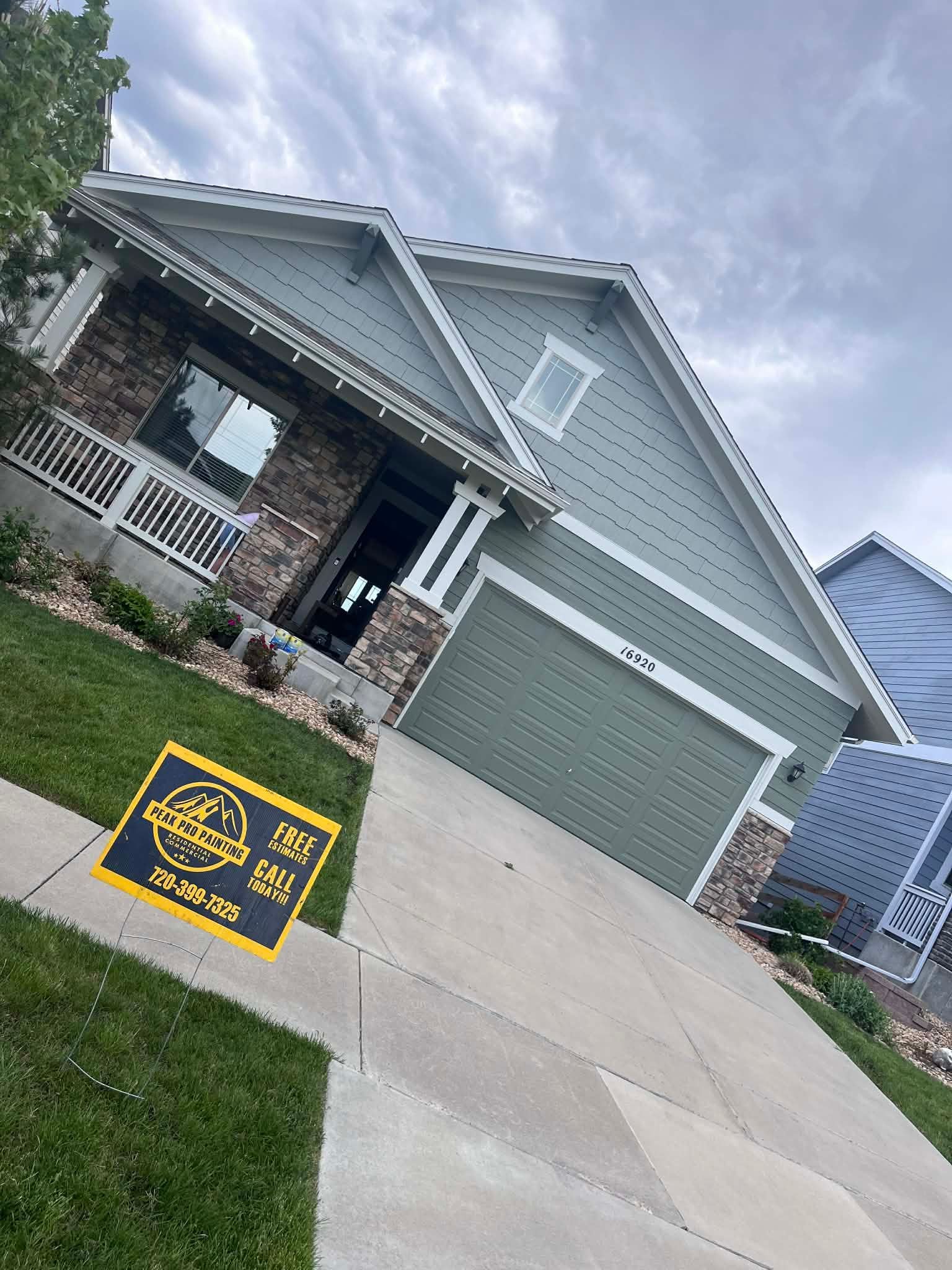 A tan and stone, single-story residential house under a cloudy sky, with a real estate sign on the front lawn.