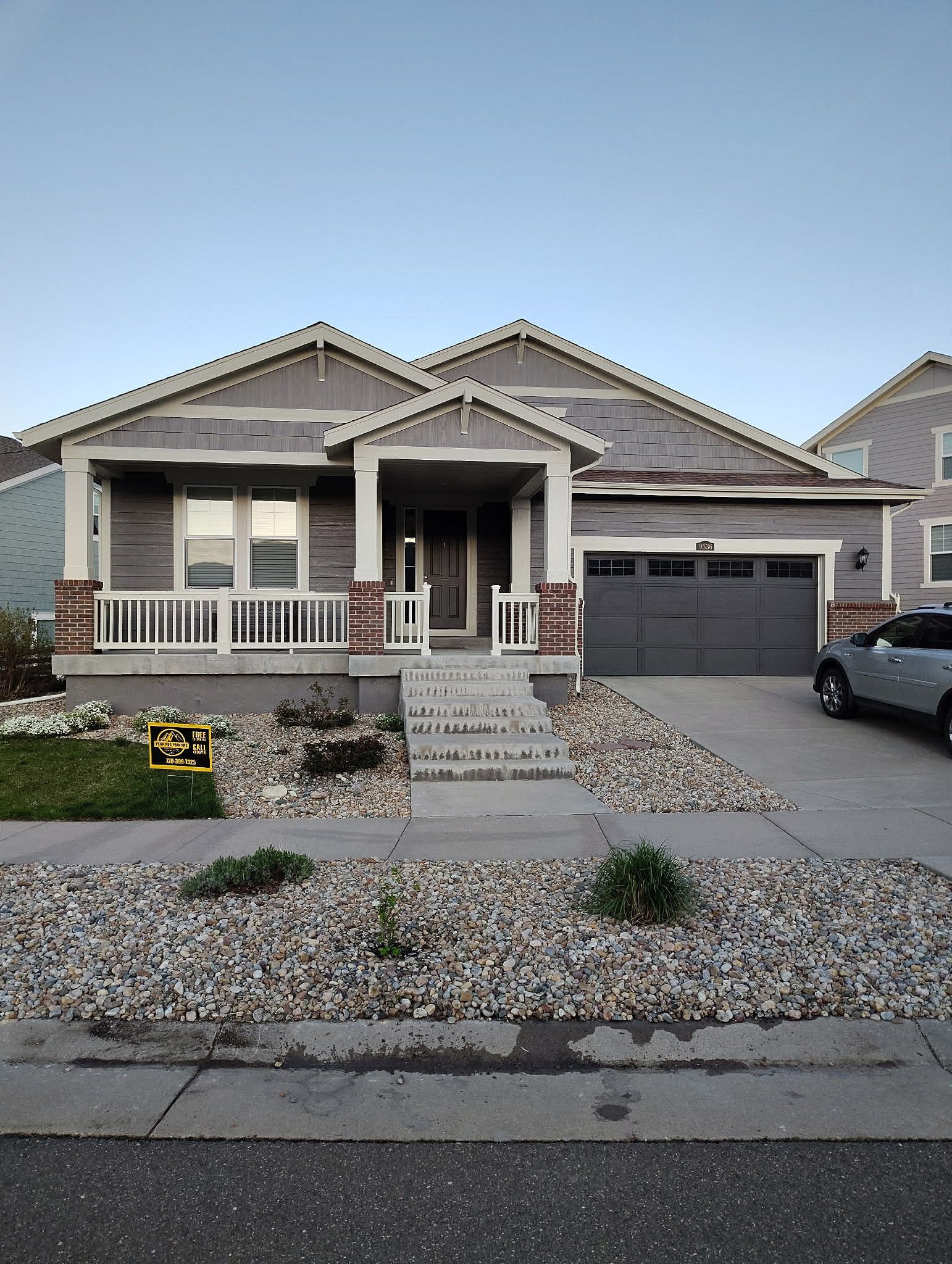 A modern, single-story house with gray siding, a front porch, and a two-car garage, featuring a gravel front yard.