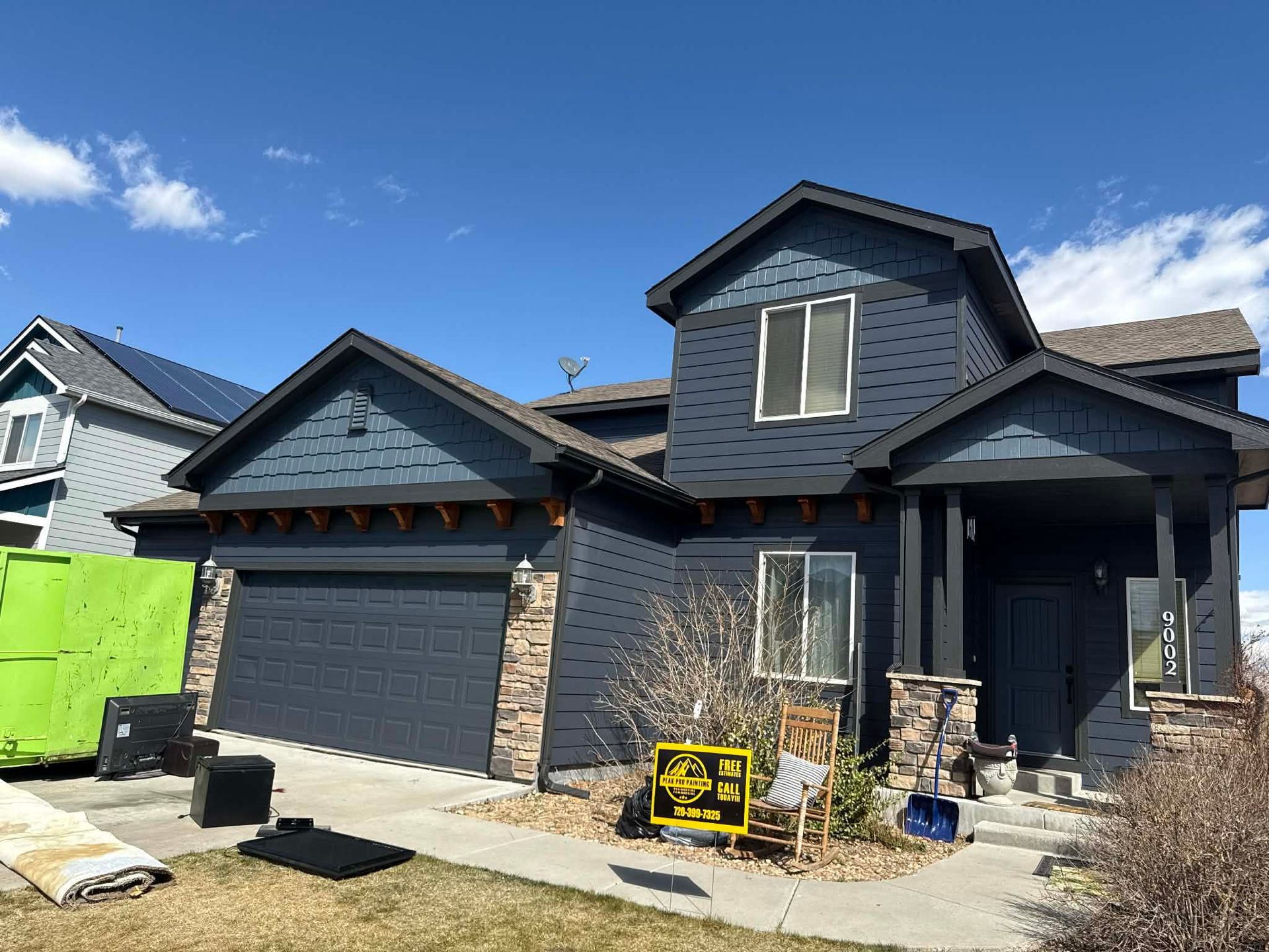 A two-story dark blue suburban house with a stone accent and an attached garage under a bright blue sky.