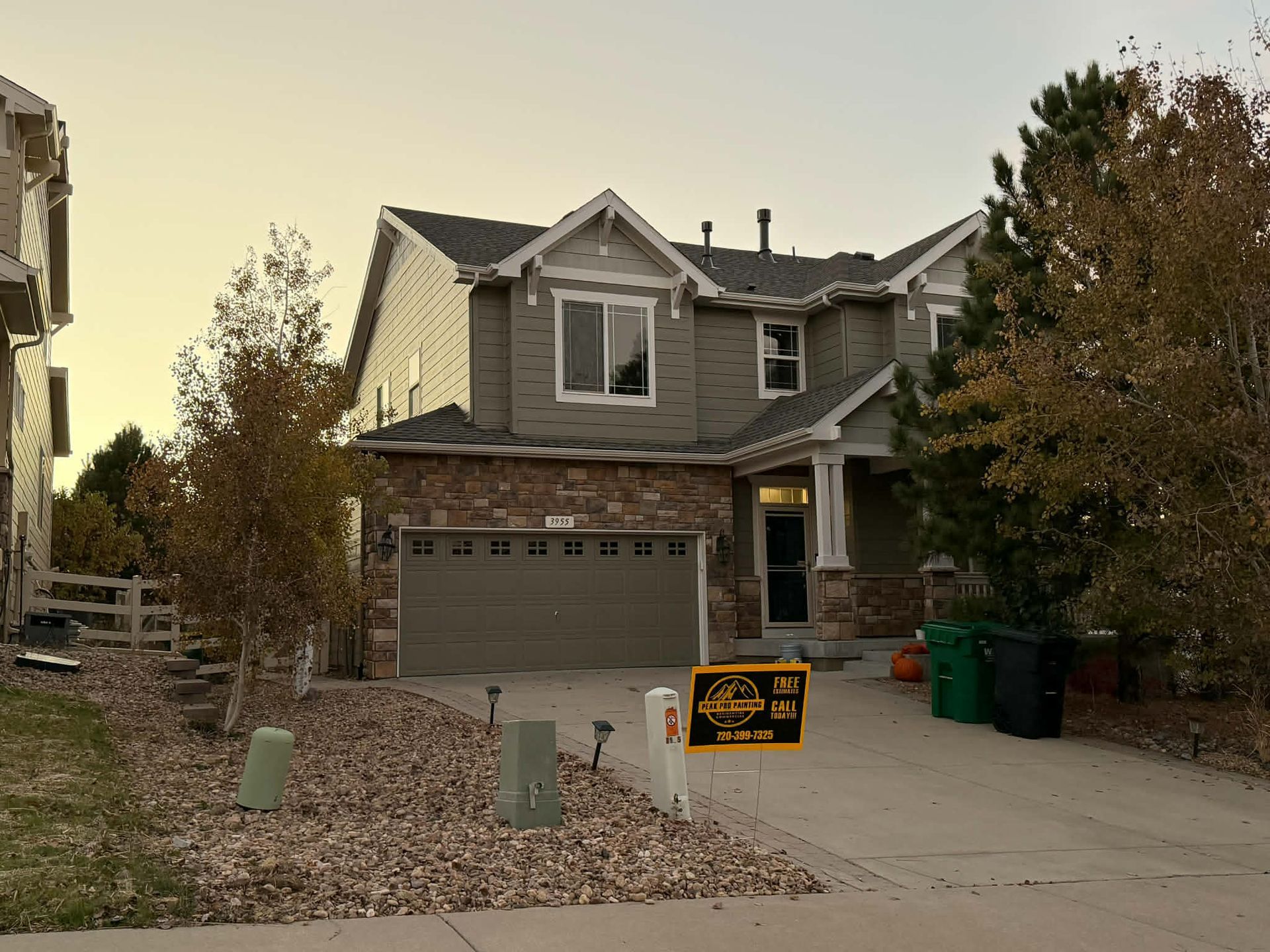 A two-story suburban house with stone siding and a garage, featuring a yellow sign on the driveway during sunset.
