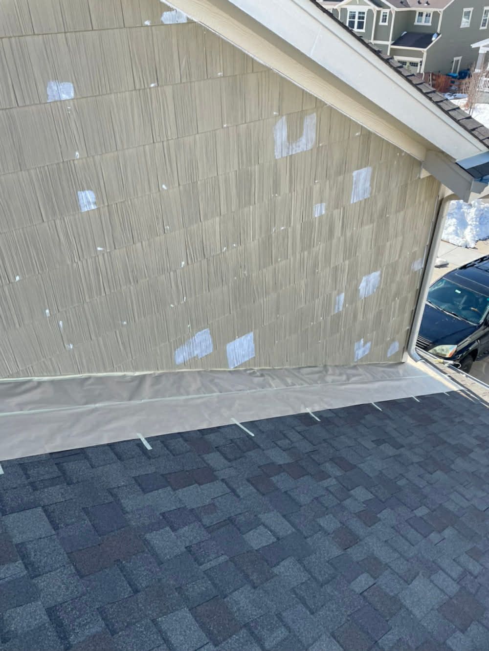 A high-angle view of a residential roof with shingles and siding under repair, featuring white tape over panel seams.