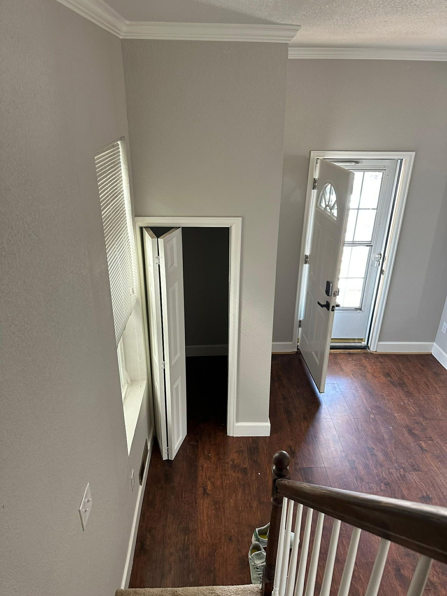 A high-angle view of a gray-walled interior entry with dark wood floors, a folding closet door, and a bright white door.
