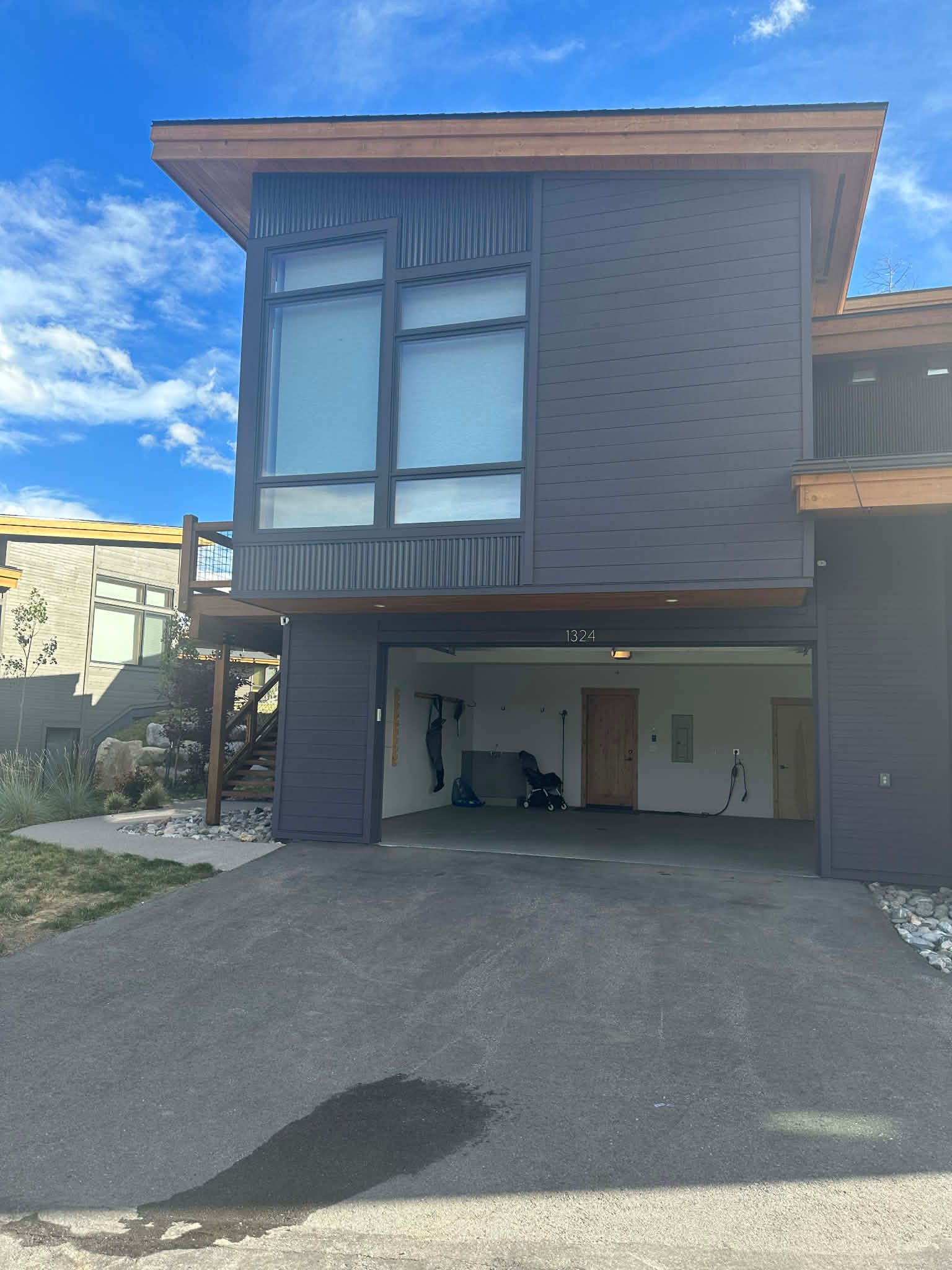 A modern house with a dark facade, large windows, and an open ground-level garage under a clear blue sky.