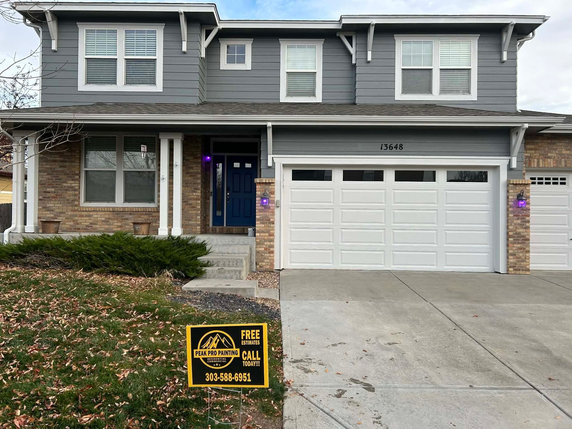 Two-story house with gray siding, stone accents, a two-car garage, and a yellow sign on the front lawn.