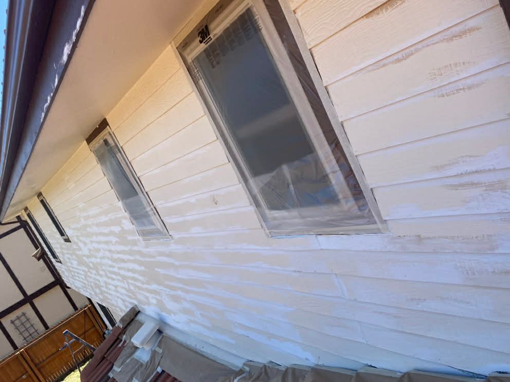 Light-colored wood siding on a house exterior during a renovation, with windows covered by protective plastic.