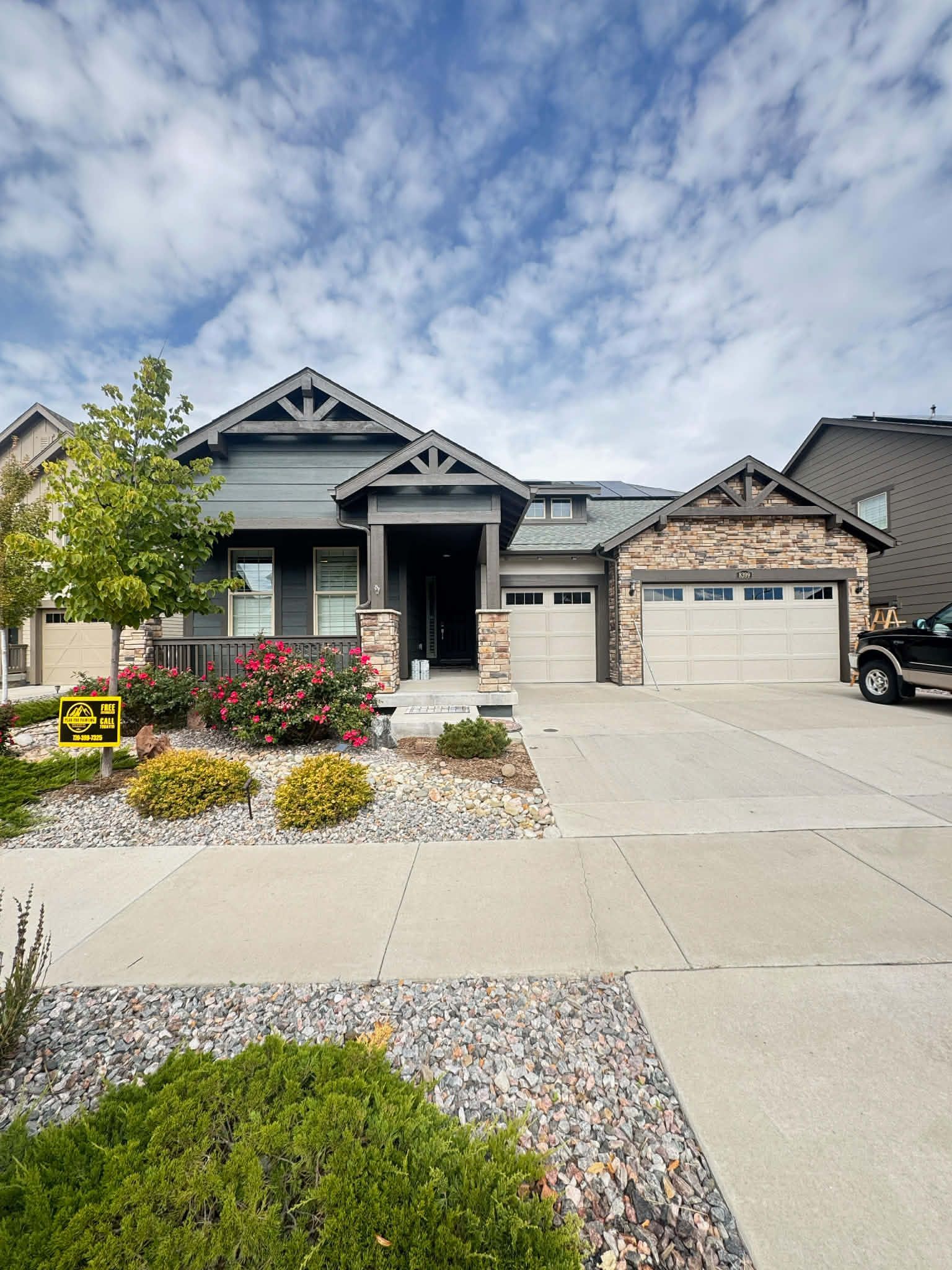 A single-story suburban home with a gray exterior, stone accents, two garage doors, and a rocky front yard garden.