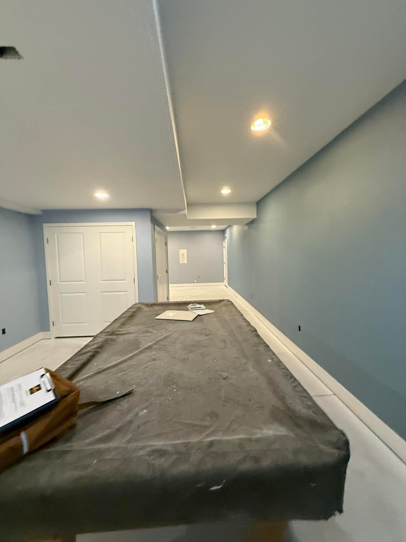 A pool table with a grey cover sits in the center of an empty room with blue walls, white doors, and recessed lighting.