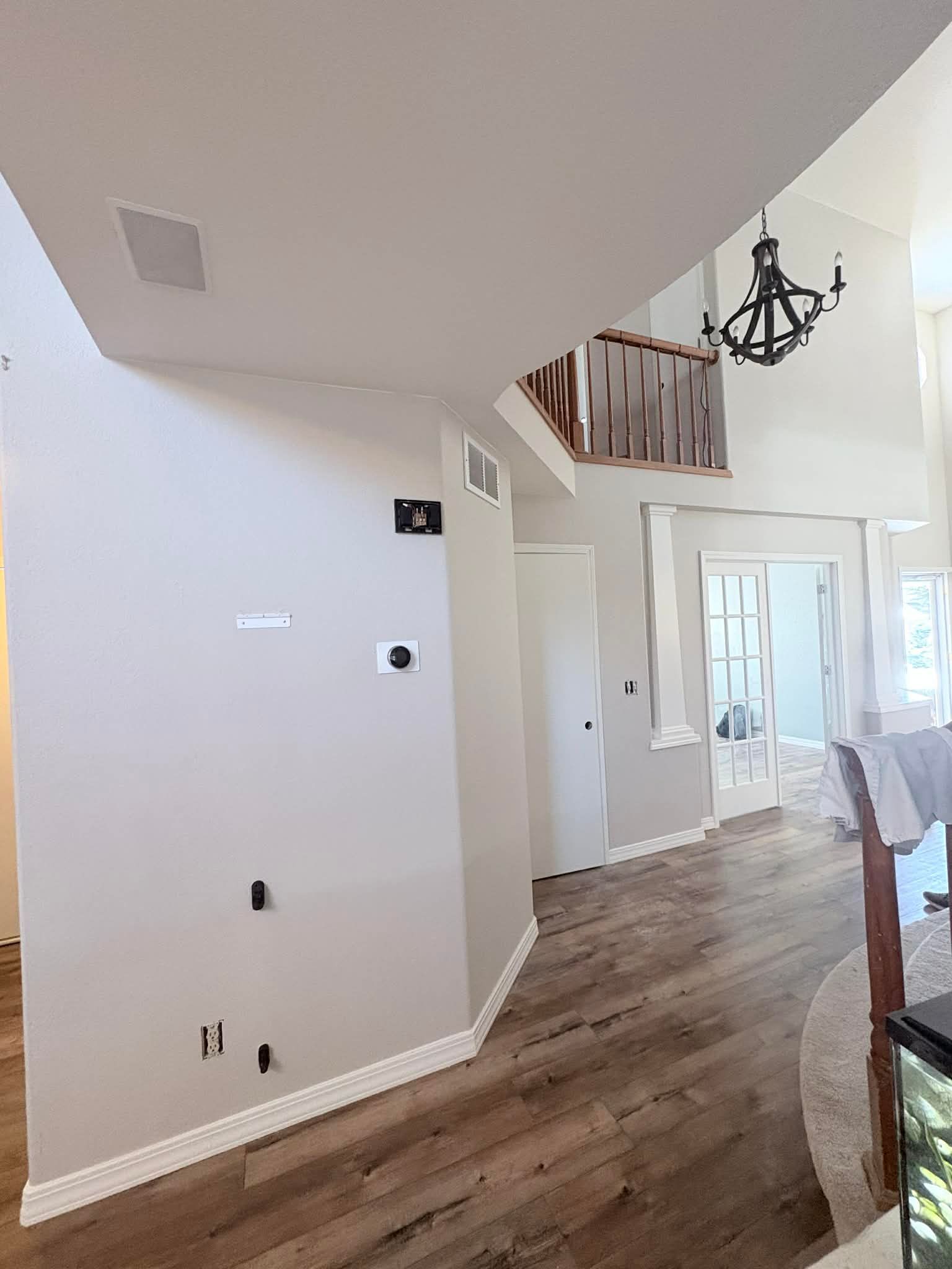 A bright, open foyer features light grey walls, wood-look flooring, a chandelier above stairs, and a glass-paned door.