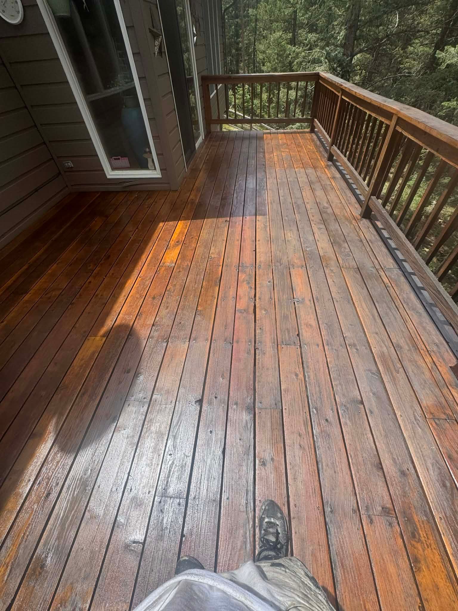 A high-angle view of a freshly stained wooden deck with vertical grooves, looking out towards a wooded area.
