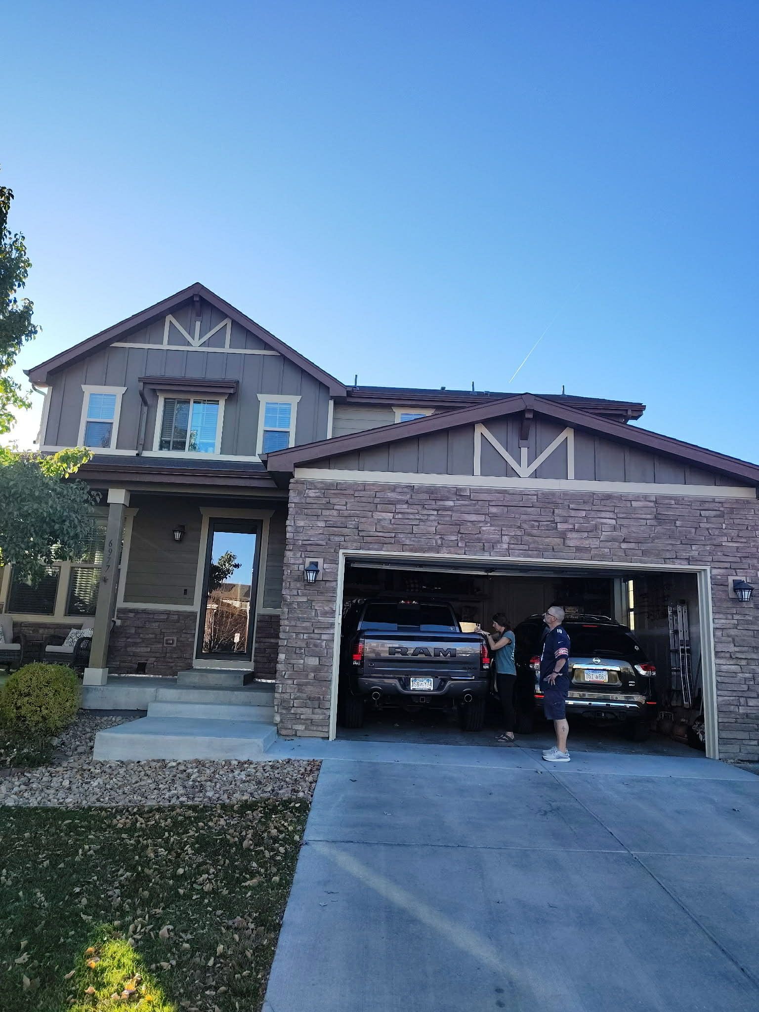 A house exterior with a two-car garage open, showing two vehicles parked inside and people standing near the driveway.