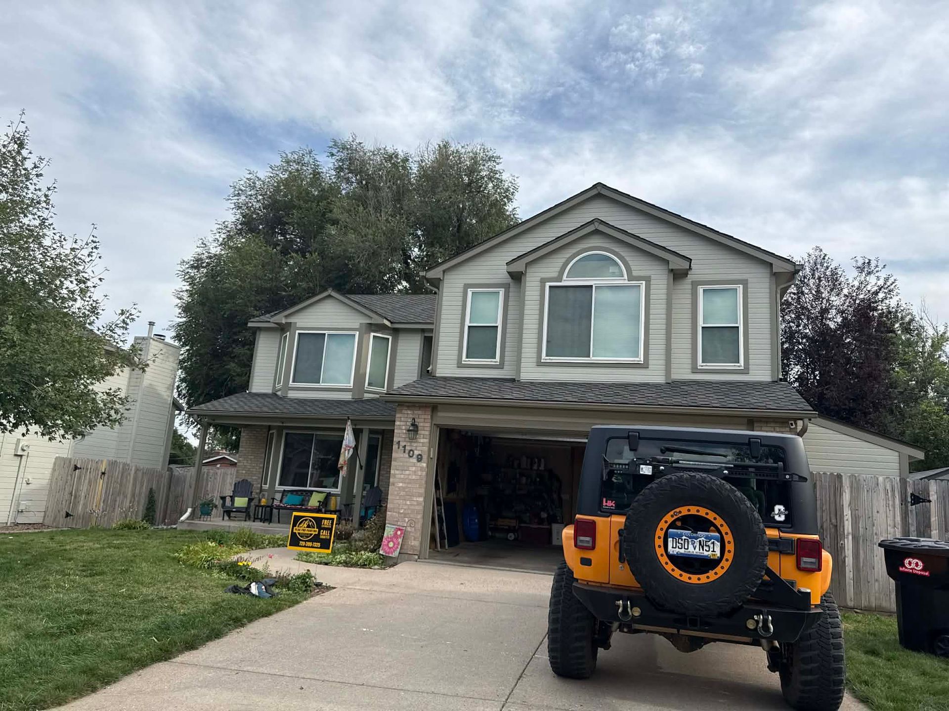 A two-story light-colored suburban house with an attached garage, featuring a yellow Jeep parked in the driveway.