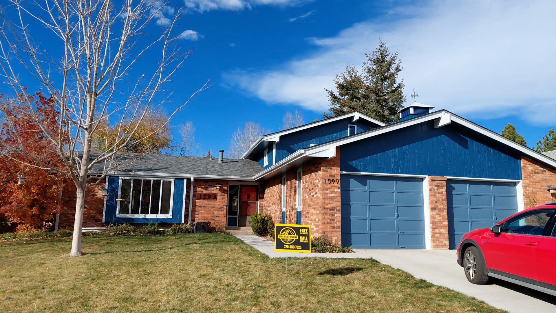 A blue and brick-sided suburban house with a double garage and a yellow sign on the front lawn.