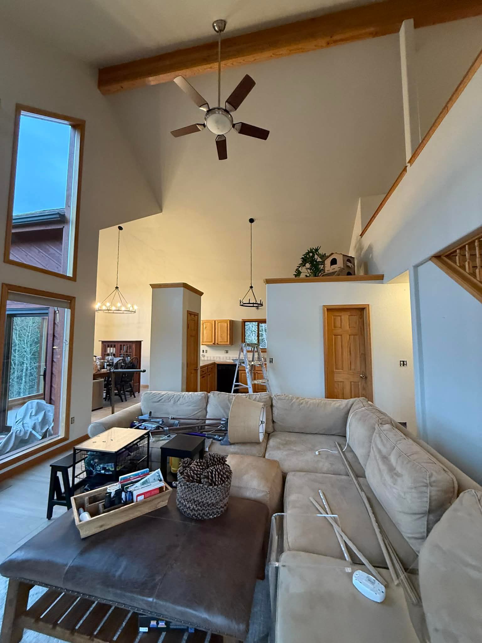 A spacious living room with a high ceiling, exposed wooden beams, a ceiling fan, and a large sectional couch.