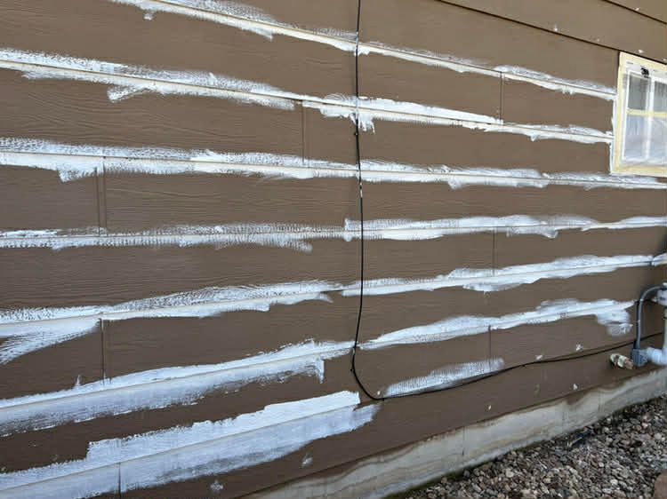 Brown siding planks with white caulk applied to the horizontal seams and a vertical joint on an exterior wall.