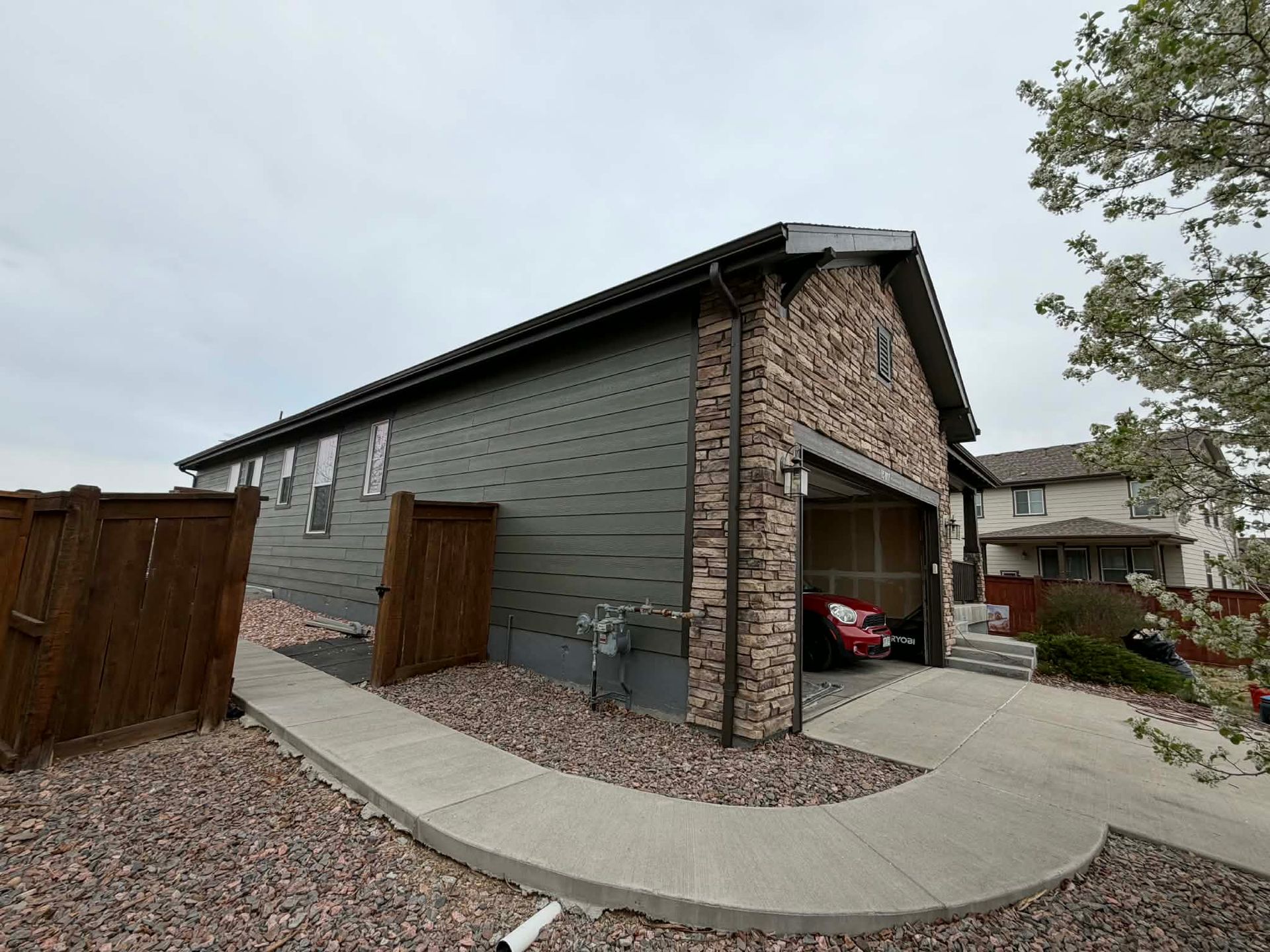 A residential house with green siding and a stone facade featuring an open garage with a car parked inside.