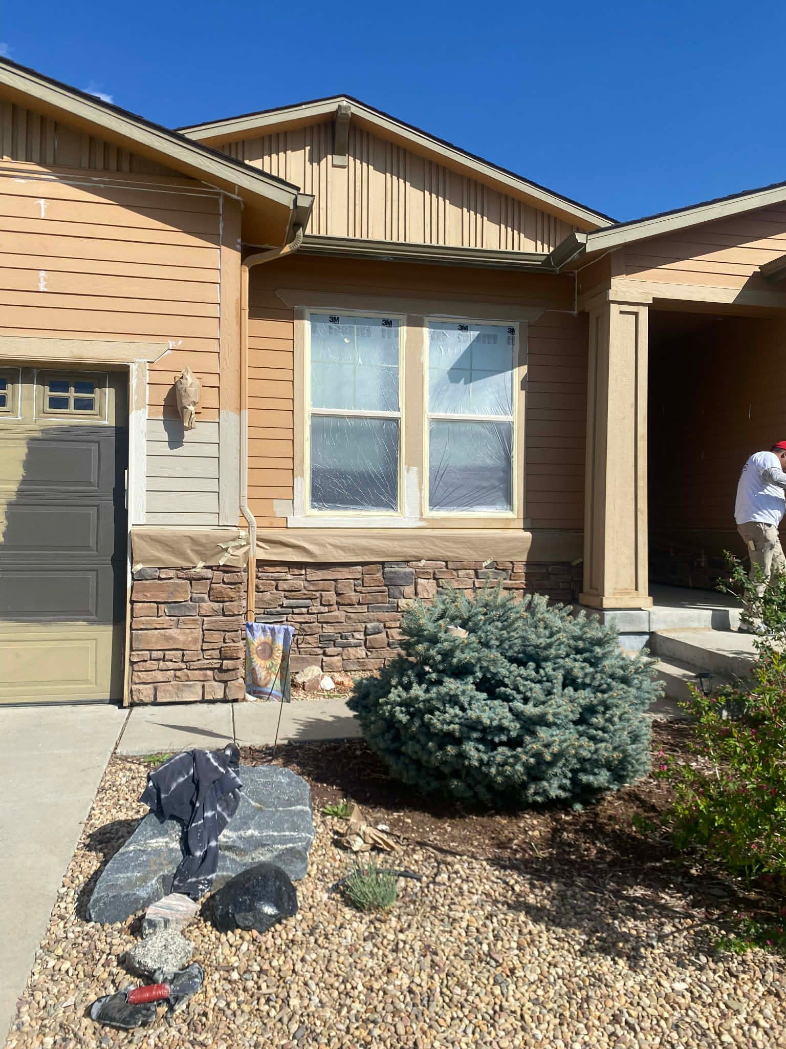 A house exterior undergoing repairs, featuring light brown horizontal siding, tan vertical siding, and a stone facade.