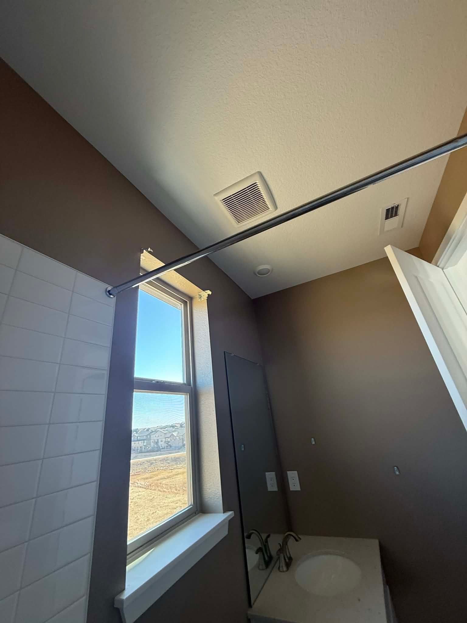A bathroom interior featuring a window, a shower curtain rod, a ceiling vent, and a vanity mirror with a sink.