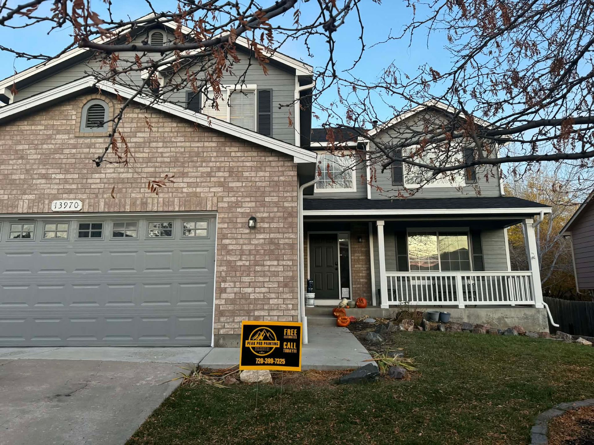 A two-story house with a brick and gray siding exterior, a front porch, and a yard sign in the driveway.