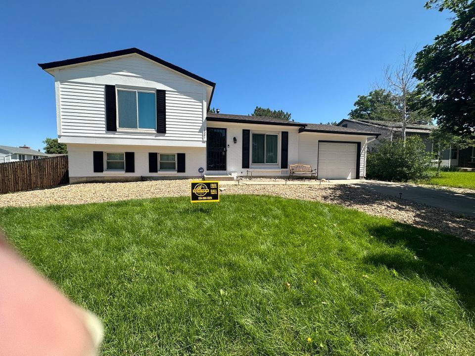 A split-level home with white siding, black trim, a garage, and a gravel front yard under a clear blue sky.