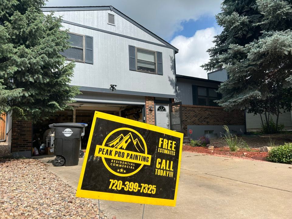 A residential house with a Peak Pro Painting yard sign in the foreground, near a driveway and trash bin.