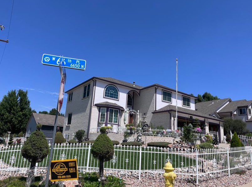 A two-story house with white siding stands behind a white fence under a clear blue sky, next to a street sign for 6th St.