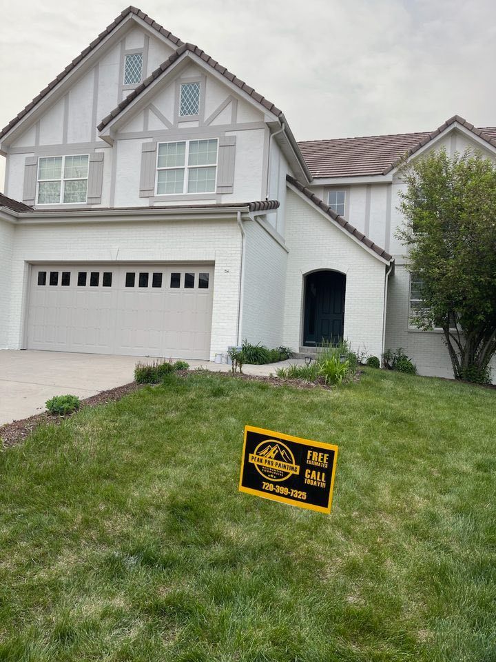 A two-story white house with a tan garage door and a yellow yard sign on a green lawn.