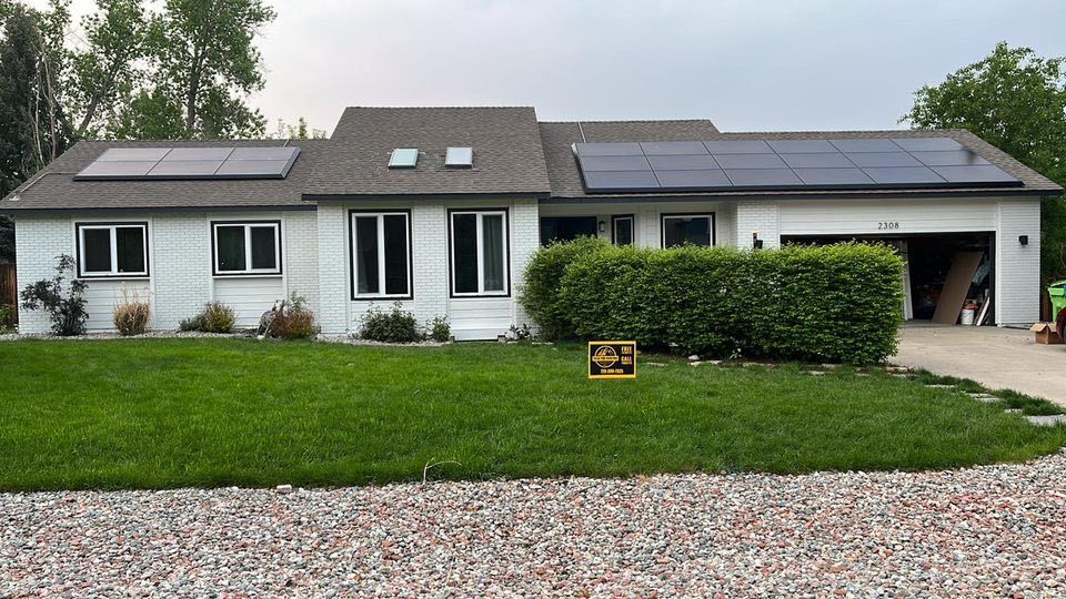 White ranch-style house with dark solar panels on a gray roof, green lawn, and a pebble driveway.