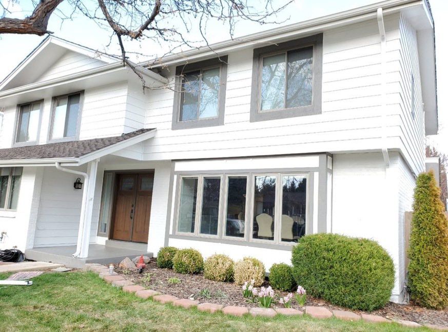A two-story house with white siding, dark window trim, a wooden front door, and a landscaped front yard.