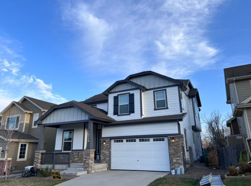 Two-story suburban house with white siding, stone accents, a two-car garage, and a porch under a blue, cloudy sky.