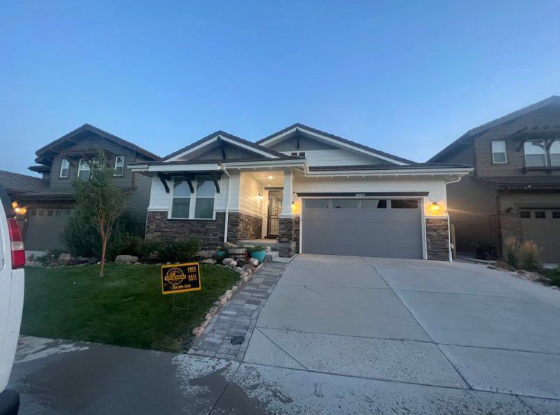 A contemporary single-story suburban house with a gray garage door, stone accents, and a paved driveway at dusk.