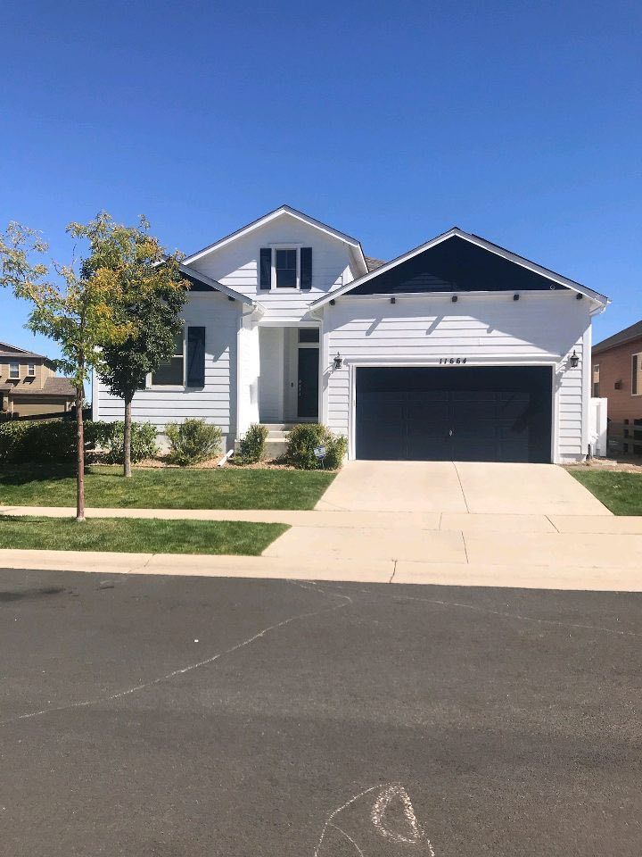 A one-story white house with a dark blue garage door, a gabled roof, and a small front yard under a clear blue sky.
