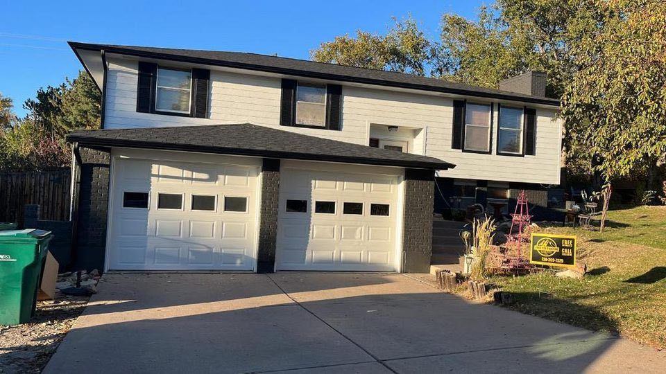A white split-level house with black trim, a two-car garage, and a concrete driveway under a clear blue sky.