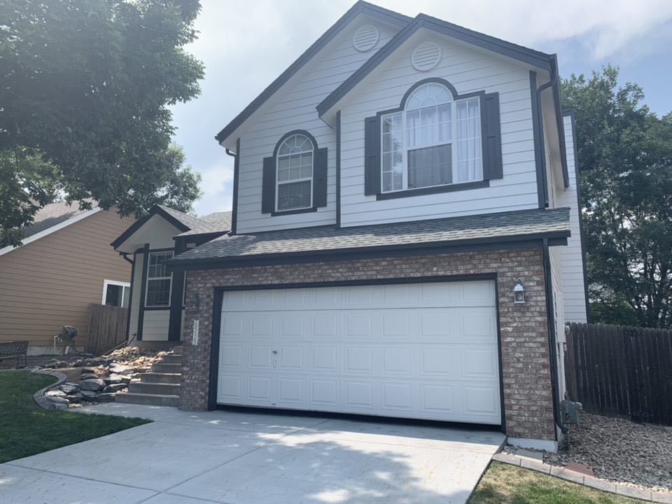 Two-story suburban house with white siding, a brick lower facade, a two-car garage, and steps leading to the front door.