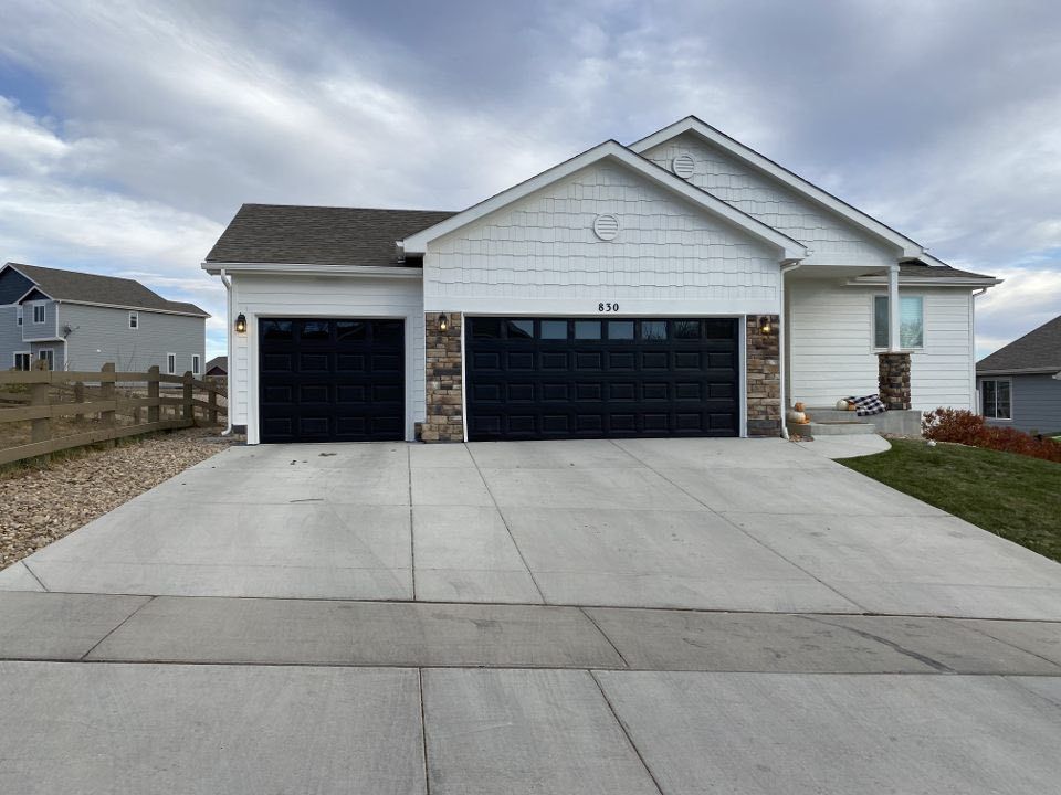 A white, suburban single-story house with a three-car garage and stone accents, viewed from the concrete driveway.