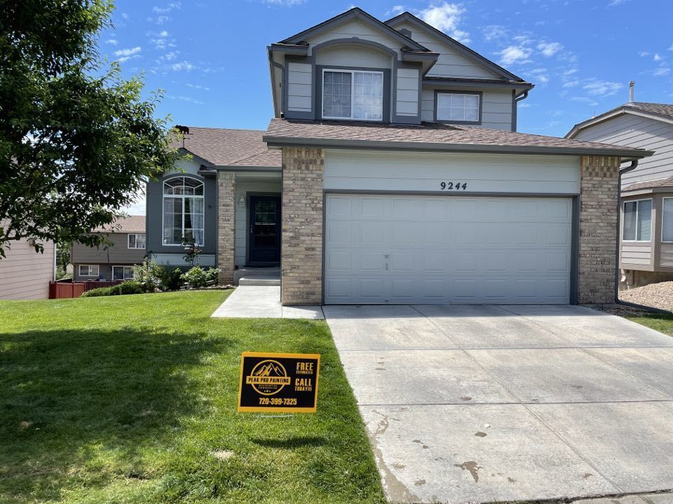 A two-story suburban house with beige siding, stone accents, and a garage, featuring a lawn sign in the front yard.