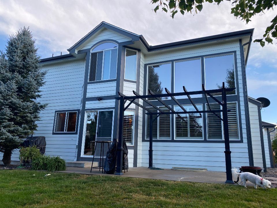 A two-story white house with dark trim and large windows, featuring a back patio with a pergola and two small dogs.