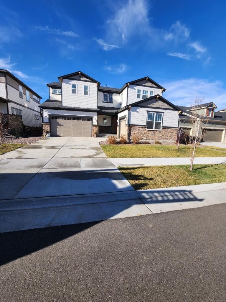 A two-story suburban house with white siding, stone accents, a multi-car garage, and a driveway under a clear blue sky.