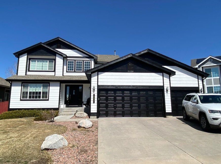 A modern two-story home with white horizontal siding, black trim, a three-car garage, and a white SUV parked in the drive.